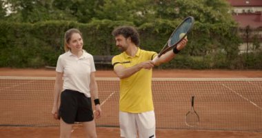 4K. Middle age man teaches a girl to play tennis on a tennis court. Summer season.