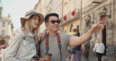 Happy multiethnic couple tourists sightseeing city with coffee. Mixed-race woman and korean man in love on honeymoon travel in european city.