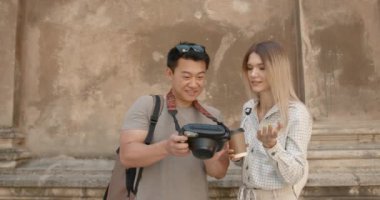 Korean man and caucasian woman looking at full frame camera screen for photo after taking pictures in middle of city. Holiday Vacation, tourist travel couple sharing good memories.