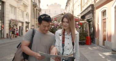 Young couple looking at map in the city. Honeymoon trip, backpacker tourist, historical city tourism, or summer holiday vacation travel concept. High Resolution.