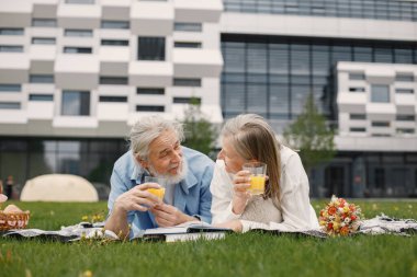 Yazın çimlerin üzerinde battaniyeye uzanmış beyaz yaşlı bir çift. Erkek ve kadın kitap okuyor ve meyve suyu içiyor. Beyaz tişörtlü kadın ve mavi erkek..