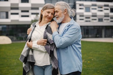 Yazın çimlerin üzerinde duran Kafkasyalı yaşlı çift. Erkek ve kadın sarılıyor. Beyaz gömlekli ve ekose battaniyeli bir kadın..