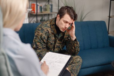 Terapi sırasında koltukta oturan asker ve psikiyatristin kesilmiş fotoğrafı. Askeri üniforma giyen adam. Psikiyatristle konuşan erkek savaşçı..