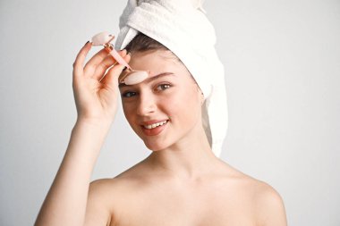 Beyaz arka planda yüzü yuvarlanan beyaz bir kadın. Kız saçını havluya sarmış. Siyahi kadın, vücut tedavisinden sonra.