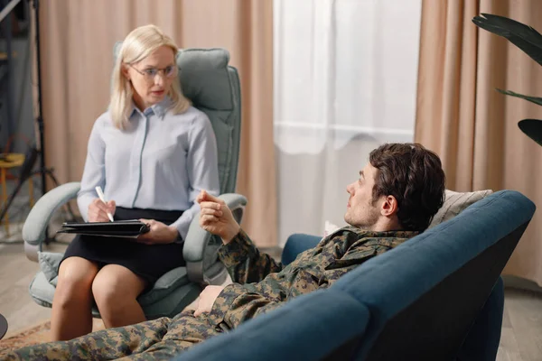 Soldier laying on couch during therapy session. Man wearing military uniform. Male warrior with ptds talking to psychiatrist.