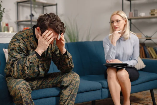 Soldier and psychiatrist sitting on couch during therapy session. Man wearing military uniform. Male warrior with ptds talking to psychiatrist.