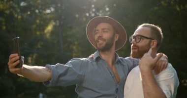 Attractive hipster bearded gay couple taking selfie in the park. Homosexual man hugging together while posing for a photo.