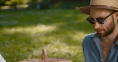 Man spending weekend time with boyfriend at summer picnic. Handsome bearded gay couple sitting on blanket and talking at date. Romance concept, lgbtq concept.