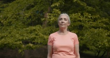 Elderly woman stretching and doing exrcise in the summer park. Sporty, healthy lifestyle on retirement.