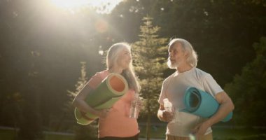 Smiling senior couple in park exercising taking a break hydrating. Healthy lifestyle , retirement.