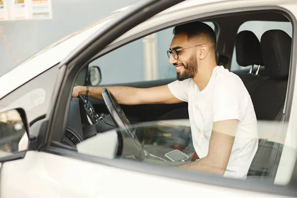 Young man in glasses polishing inside his car with a rug. Man wearing white t-shirt. Indian man wiping his white vehicle.