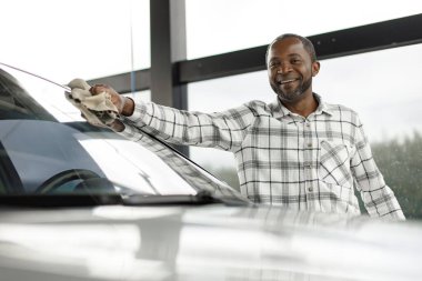 Man washing luxury car on a car wash with a rag. Black man wiping his car. Man wearing plaid shirt, smiling.