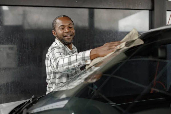 Man washing luxury car on a car wash with a rag. Black man wiping his car. Man wearing plaid shirt, smiling.