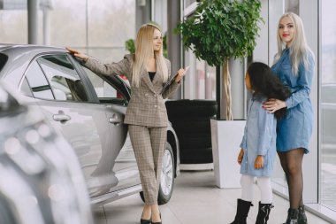 Family in a car salon. Woman buying the car. Little african girl with mther. Manager with clients.