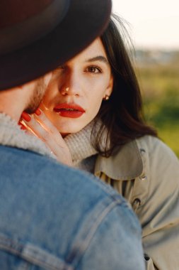 Kırmızı dudaklı bir kadına odaklan. Moda elbiseli romantik bir çift sarılıyor. Ceketli bir adam ve kadın ceketi..