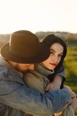 Kameraya bakan bir kadına odaklan. Moda kıyafetleri içinde piknik halısında oturan romantik bir çift. Ceketli bir adam ve kadın ceketi..