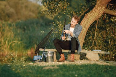 Adam bir ağacın yanında oturuyor ve balık tutuyor. Balıkçı işine yoğunlaşmıştı. Mavi gömlekli adam..