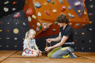 Eğitmen müşteri küçük kızın içeri tırmanma merkezinde emniyet kemeri takmasına yardım ediyor. Küçük kız, çocuk eğlence merkezinde kaya tırmanışı yapıyor. Sarışın.