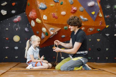 Eğitmen müşteri küçük kızın içeri tırmanma merkezinde emniyet kemeri takmasına yardım ediyor. Küçük kız, çocuk eğlence merkezinde kaya tırmanışı yapıyor. Sarışın.