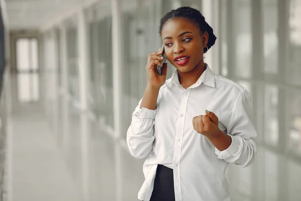 Black girl in the office. Woman in a white shirt. Lady use the phone.