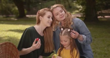 Güzel ve mutlu bir çift beyaz lezbiyen ekose üzerinde oturup tatlı kızıyla temiz havada eğleniyorlar. Aile zamanı kavramı, lgbt insanları ve yaşam tarzları.