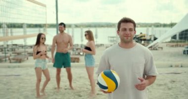 Genç adam topu parmağında oynatıyor. Arkadaşlar voleybol oyuncuları kalenin arkasında duruyor.