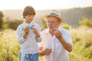 Küçük kaşif ve büyükbabasının bir tarlada iki oyuncak uçakla oynamalarının portresi. Oğlan ve büyükbaba yazın birlikte vakit geçiriyorlar. Esmer çocuk ve çizgili gömlek giyen adam..
