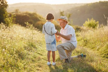 Küçük çocuğun ve büyükbabasının tarlada dikilip konuşurken çekilmiş bir fotoğrafı. Oğlan ve büyükbaba yazın birlikte vakit geçiriyorlar. Esmer çocuk ve çizgili gömlek giyen adam..