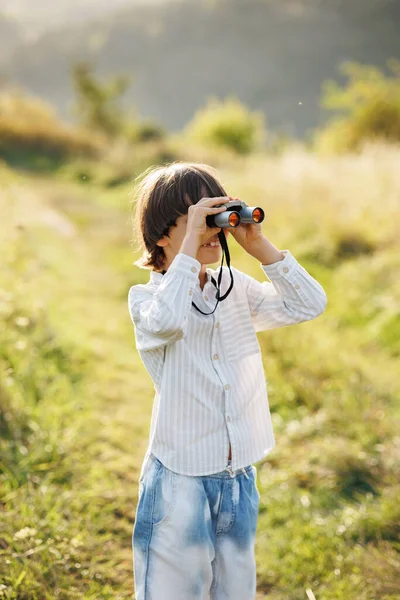 stock image Portrait of little explorer with binoculars in a field. Little caucasian boy looking through a binoculars in a field at summer. Brunette boy wearing striped shirt.