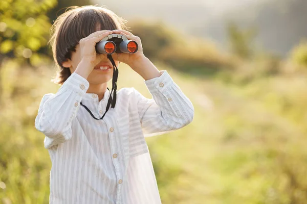 Portrait of little explorer with binoculars in a field. Little caucasian boy looking through a binoculars in a field at summer. Brunette boy wearing striped shirt.