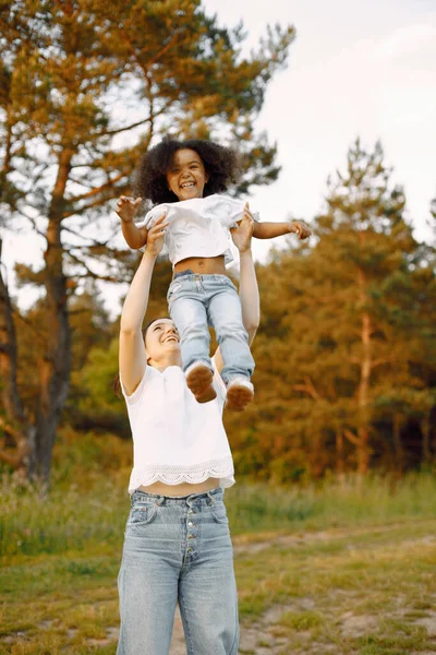 stock image Photo of caucasian mother twirling her african american daughter outdoors. Girl has black curly hair. Mother and daugher wearing white t-shirts.