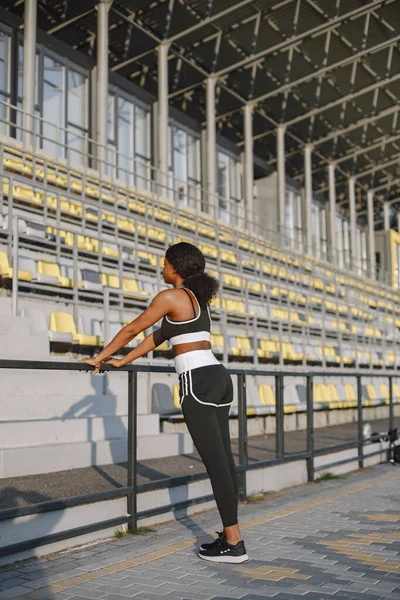 African american fitness model training outdoors. Woman wearing black sportswear. Woman training near stadium.