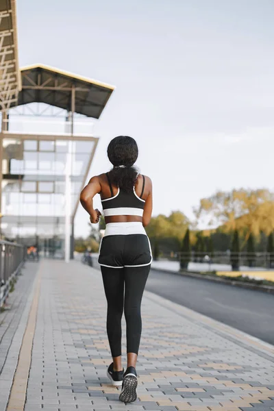 African american fitness model jogging outdoors. Woman wearing black sportswear. Woman running near stadium.