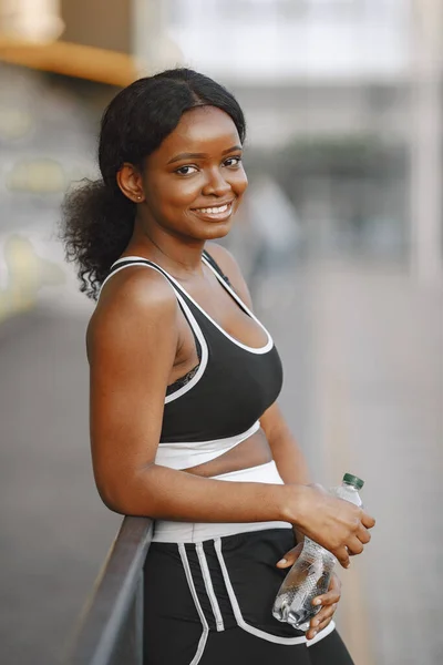 African american fitness model training outdoors. Woman wearing black sportswear. Woman looking in a camera and smiling.