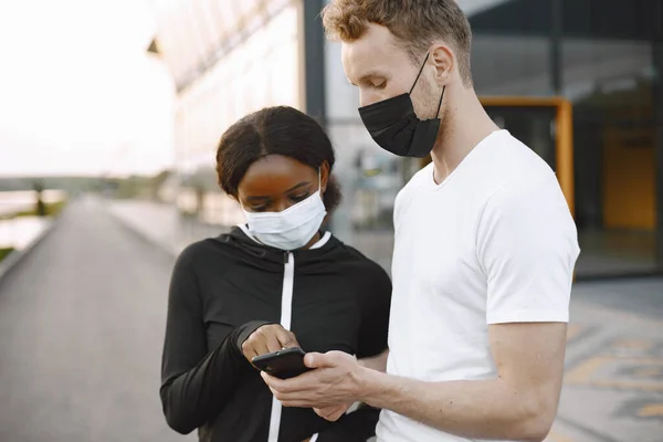 非洲裔美国人健身模特儿和白人男人在户外训练时看着手机 穿着黑色运动服的女人戴口罩的夫妻 — 图库照片