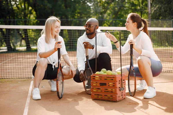 女の子の友達はテニスのレッスンを受けている 黒人のコーチが話し 遊び方を説明する 屋外遊び場 — ストック写真