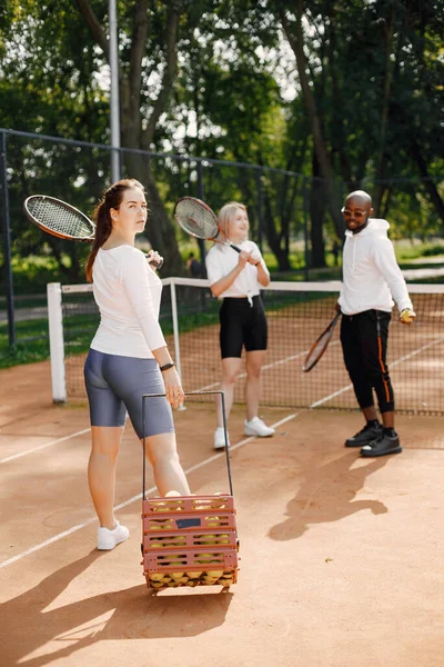 女の子の友達はテニスのレッスンを受けている 黒人のコーチが話し 遊び方を説明する 屋外遊び場 — ストック写真