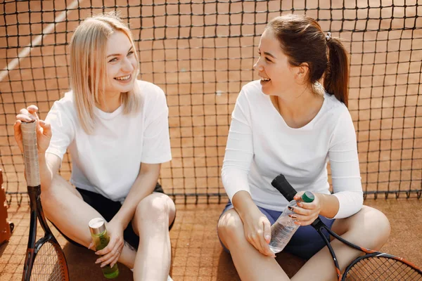 2人の若い女性がテニスネットに座っている ゲームの後に会話を持つ スポーツ レジャー — ストック写真