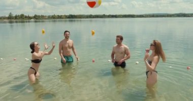 Yaz günü gölde top oynayan ve eğlenen bir grup genç arkadaş. Arkadaşlık, göl kenarı, yaz tatili, tatiller ve insanlar konsepti.