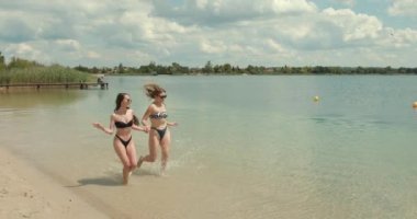 Yaz tatilleri, arkadaşlık konsepti. Genç mutlu kızlar denizde tatilin tadını çıkarıyorlar. Kumsalda koşan ve gülümseyen arkadaşlar.