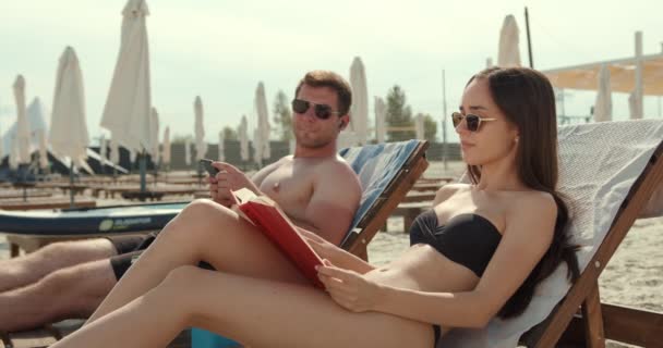 Pareja Vacaciones Verano Resort Mujer Joven Lee Libro Mientras Relaja — Vídeos de Stock