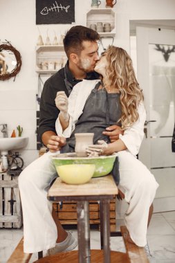 Mutual creative work. Young beautiful couple in casual clothes and aprons. People creating a bowl on a pottery wheel in a clay studio.