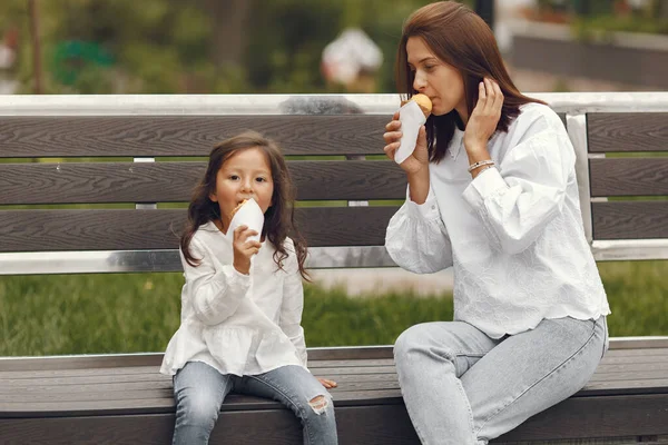 Family in a city. Little girl eats ice cream. Mother with daughter sitting on a bench.