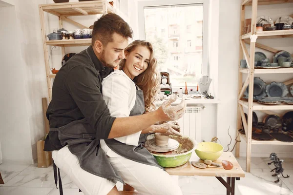 stock image Mutual creative work. Young beautiful couple in casual clothes and aprons. People creating a bowl on a pottery wheel in a clay studio.