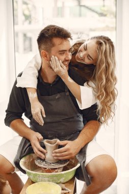 Ortak yaratıcı çalışma. Günlük giysiler ve önlükler içinde genç ve güzel bir çift. İnsanlar kilden bir stüdyoda çömlek çarkında kase yapıyorlar..
