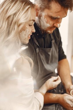 Ortak yaratıcı çalışma. Günlük giysiler ve önlükler içinde genç ve güzel bir çift. İnsanlar kilden bir stüdyoda çömlek çarkında kase yapıyorlar..