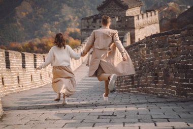 beautiful young couple running and jumping at the Great Wall of China. Newly married couple on their honemoon to Great Wall near Beijing China. Stylish couple exploring one of the wonders of the world clipart