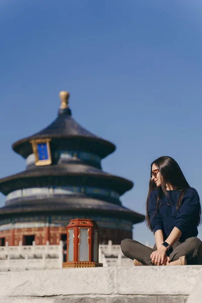 stock image brunette girl sitting on the steps by temple of heaven in China. Brunette girl enjoying chinese architecture while sitting on the steps and relaxing. Caucasian tourist taking a break from exploring