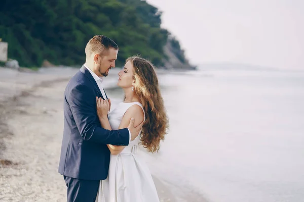 年轻貌美的长发新娘在她年轻的丈夫 在海滩上白色礼服 — 图库照片