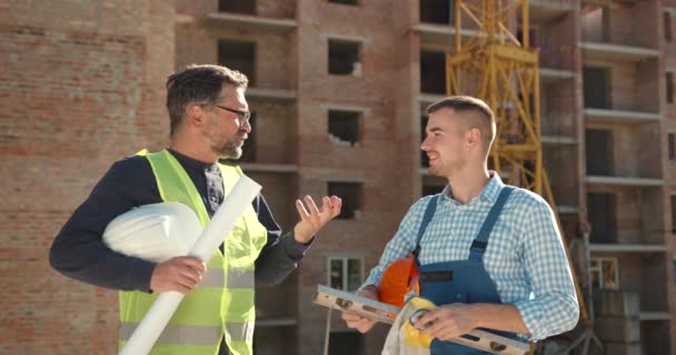 Dva Stavební Dělníci Přilbách Reflexní Vesty Diskutují Inženýrských Plánech Staveništi — Stock video